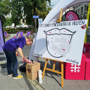 Ein Mann bereitet Farbe für eine Leinwand vor, die Menschen dazu auffordert, ihren Fingerabdruck mit Farbe darauf zu hinterlassen