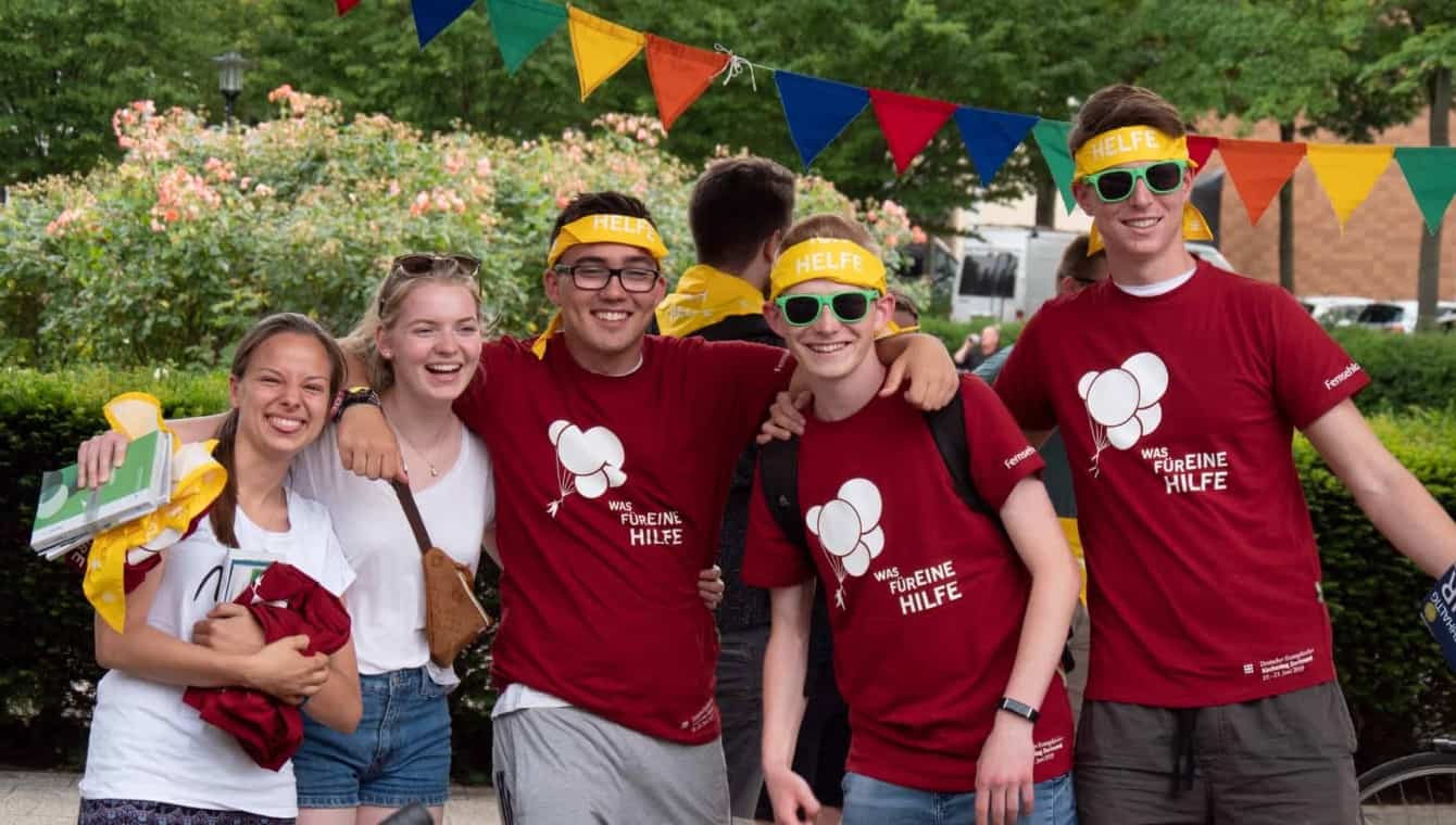Jugendliche Helfende beim Kirchentag in Dortmund 2019 haben sich zum Gruppenfoto aufgestellt, 2 Mädchen im weißen Shirt und drei Jungen im roten Helfer-Shirt und mit dem gelben Helferhalstuch als Stirnband 